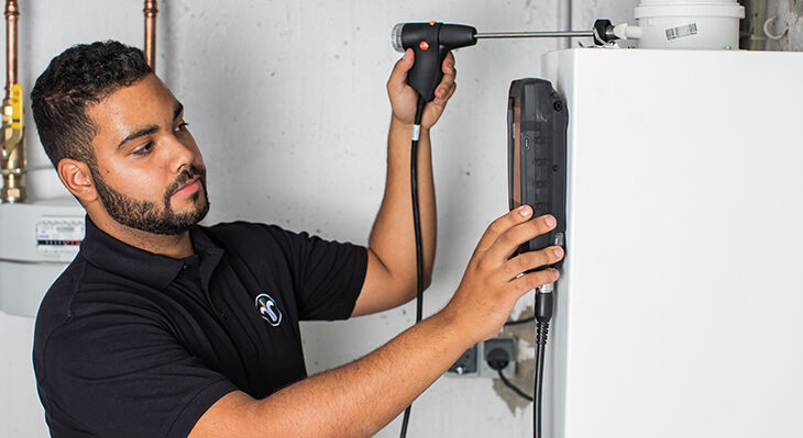 Das Foto zeigt einen Schornsteinfeger, der an einer Heizungsanlage mit einer Sonde die Abgase misst.