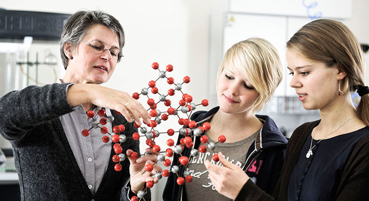 Das Bild zeigt eine Lehrerin dabei wie sie zwei Sch&uuml;lerinnen molekulare Zusammenh&auml;nge anhand eines Modells erkl&auml;rt.